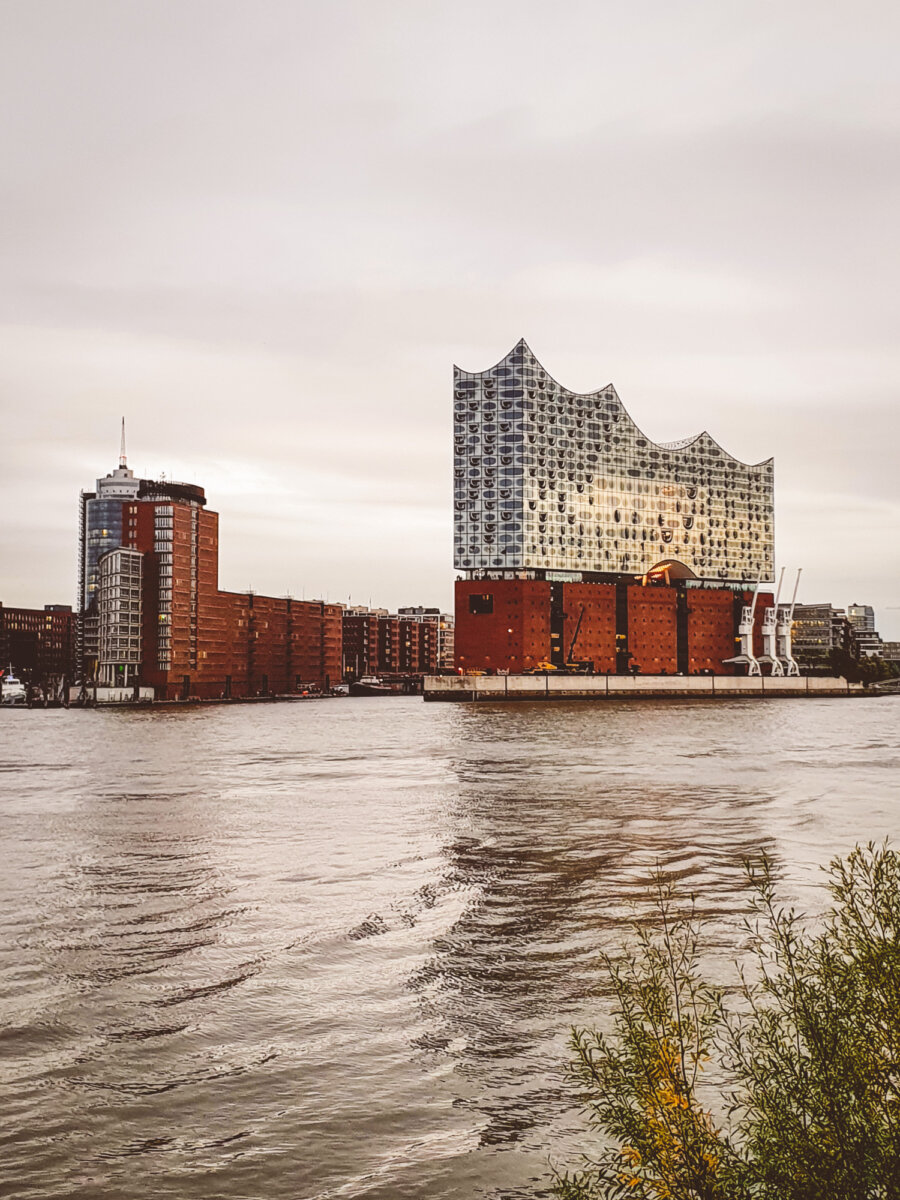 Elbphilharmonie in Hamburg am Wasser bei bewölktem Himmel, modernes Glasgebäude auf historischem Backsteinsockel.
