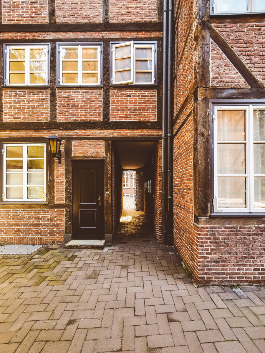 Fachwerkhaus mit schmalem Durchgang, gepflasterter Hof und offenen Fenstern im Sonnenlicht.