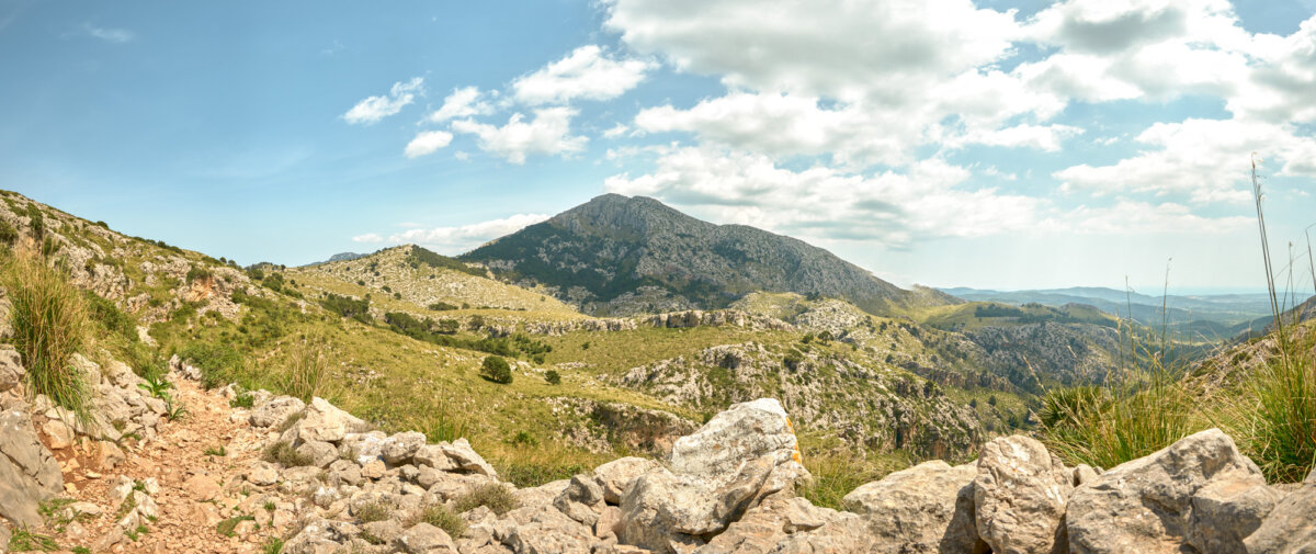 Felsiger Wanderpfad in bergiger Landschaft unter blauem Himmel mit einigen Wolken.