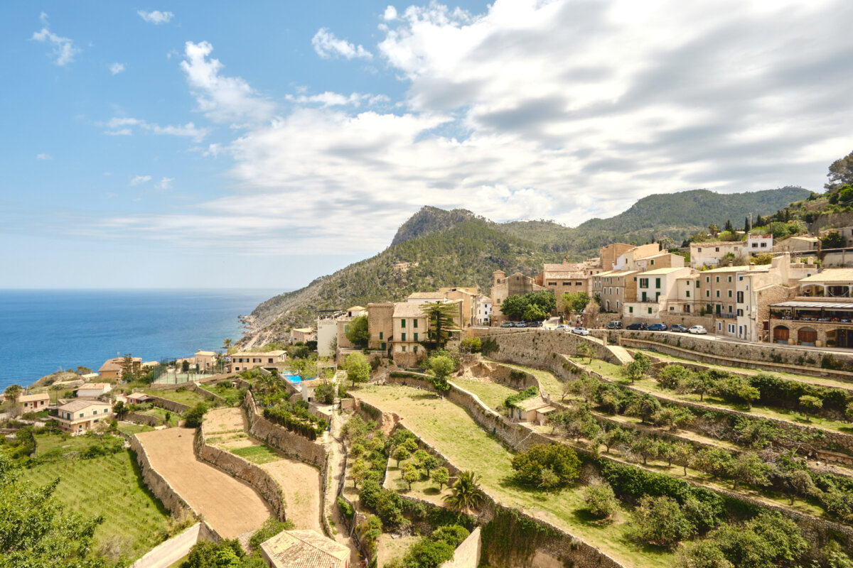 Mittelmeer-Küstenlandschaft von Banyalbufar, Mallorca, mit Terrassenfeldern und traditionellen Gebäuden bei klarem Himmel.