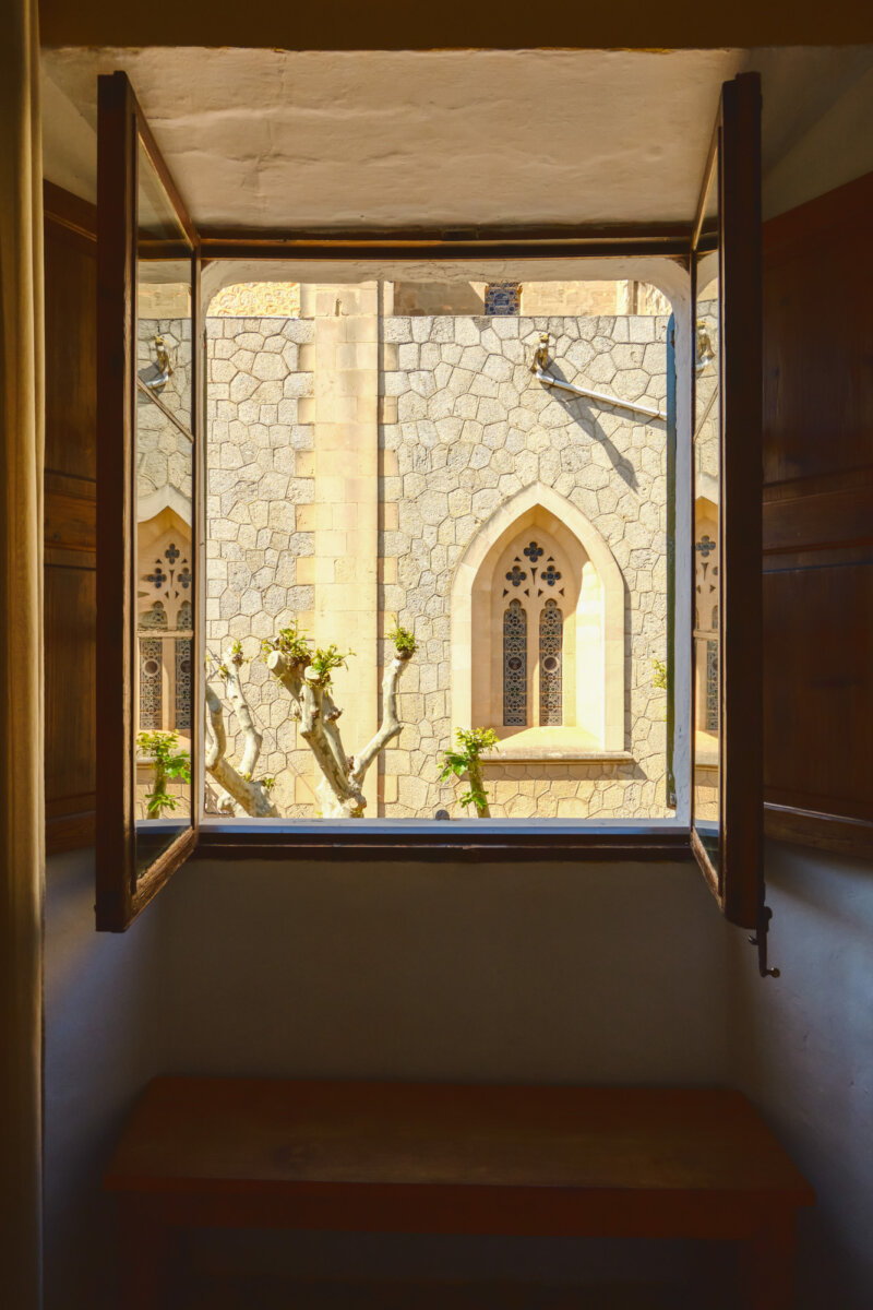 Geöffnete Fensteransicht zeigt gotische Fenster und Steinmauer eines gegenüberliegenden Gebäudes bei Tageslicht.