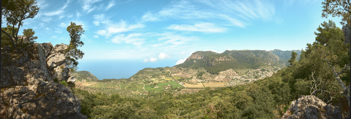 Panorama von Bergen und Tälern mit blauem Himmel und Wolken, umliegende Vegetation und Dörfer in der Ferne.