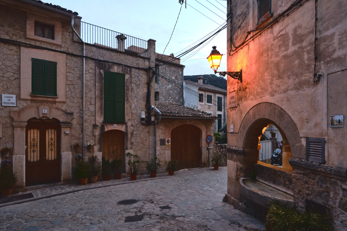 Pittoreske Altstadtgasse bei Abenddämmerung, mit beleuchteter Straßenlaterne und historischen Steingebäuden.