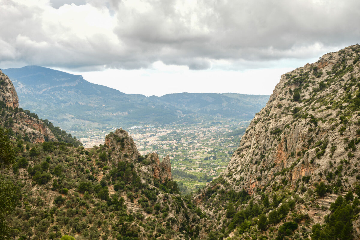Blick auf ein grünes Tal mit Felsen und Bergen unter bewölktem Himmel auf Mallorca.