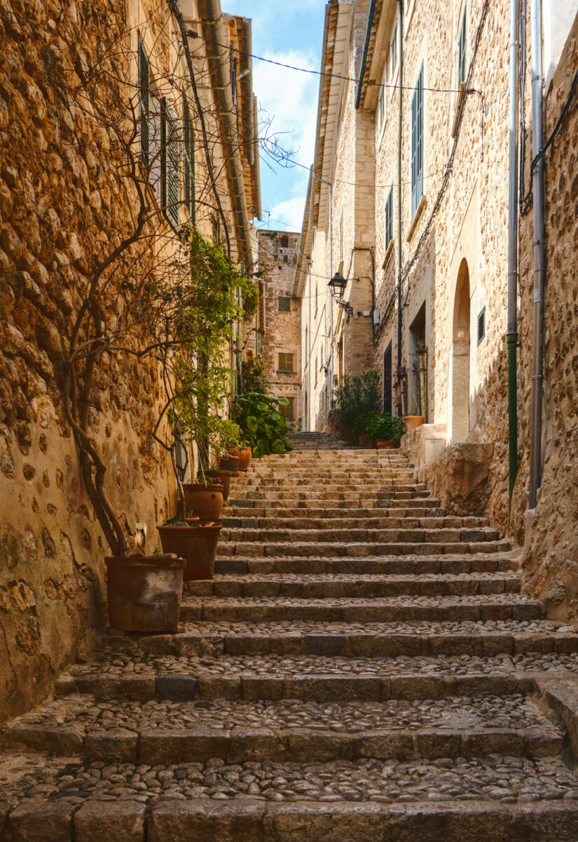 Steintreppe in enger Gasse mit Pflanzen in Töpfen, umgeben von alten Gebäuden.