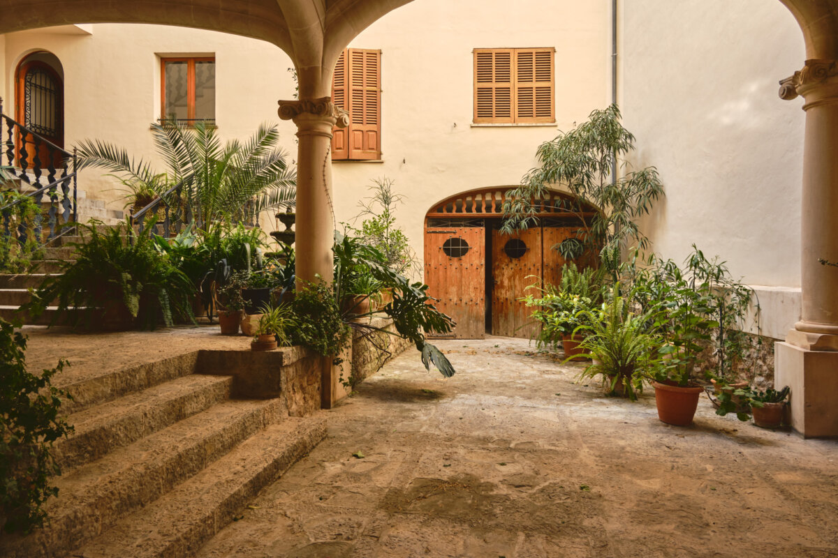 Historischer Innenhof mit Pflanzen und alten Holztüren, umgeben von Steinsäulen und Treppen.