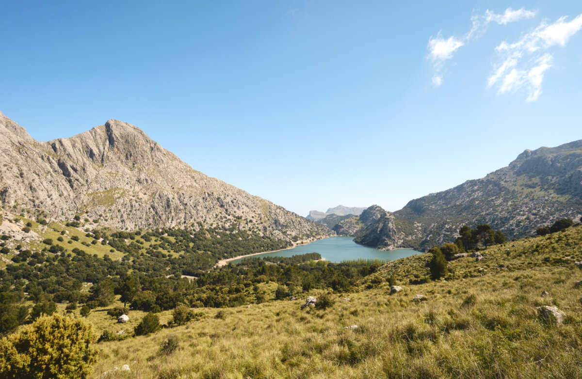 Berglandschaft mit grünem Tal und blauem See unter klarem Himmel auf Mallorca.