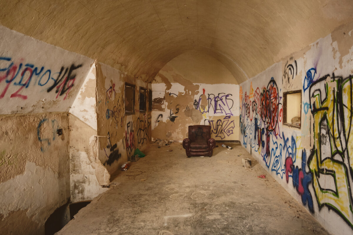Verlassener Raum mit Graffiti an den Wänden und einem alten, braunen Sessel in der Mitte der Szene.