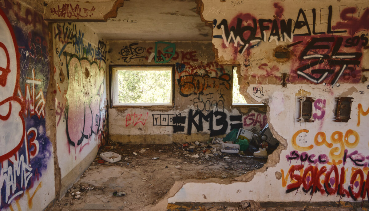Verlassenes, graffiti-bedecktes Gebäude mit zerstörten Wänden und Müll auf dem Boden, eine Öffnung zeigt grüne Natur.