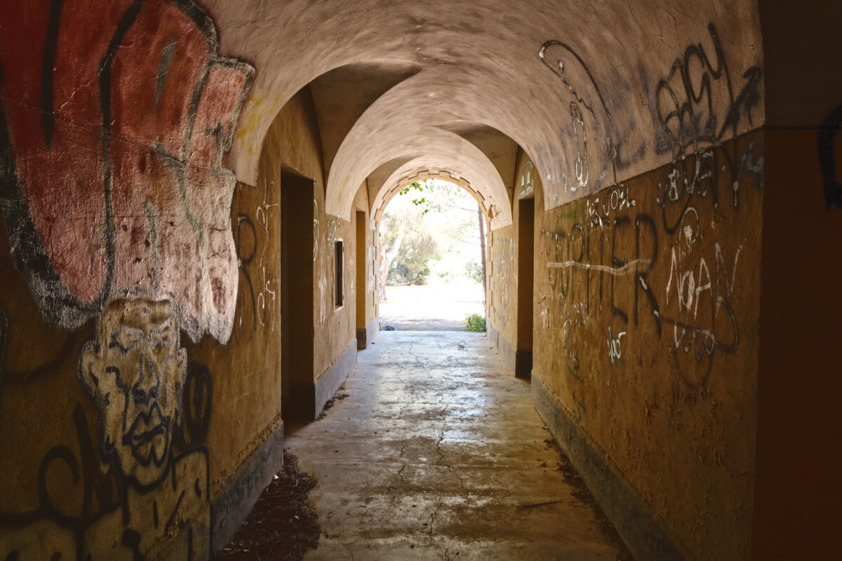 Verlassener, mit Graffiti bedeckter Tunnel mit bogenförmigen Decken, Sonne scheint am Ende durch.