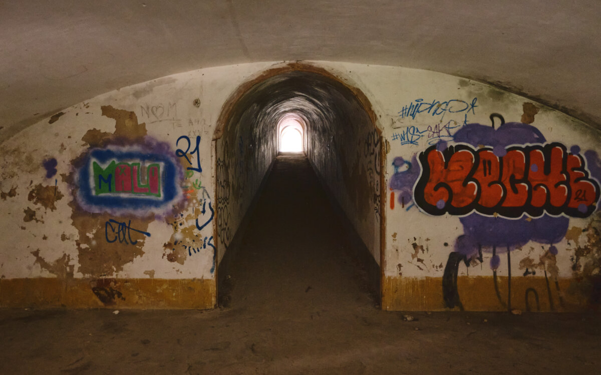 Verlassener, dunkler Tunnel mit Graffiti auf den Wänden. Ein heller Lichtschein am Ende des Tunnels.