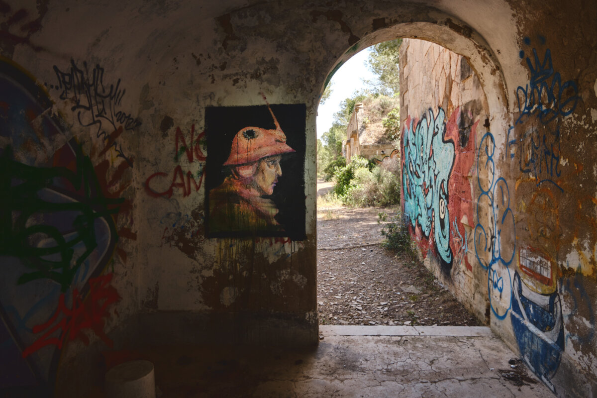 Gemalter Ritterhelm an Wand mit Graffiti in verfallenem Gebäude, Blick ins Freie durch Türbogen.
