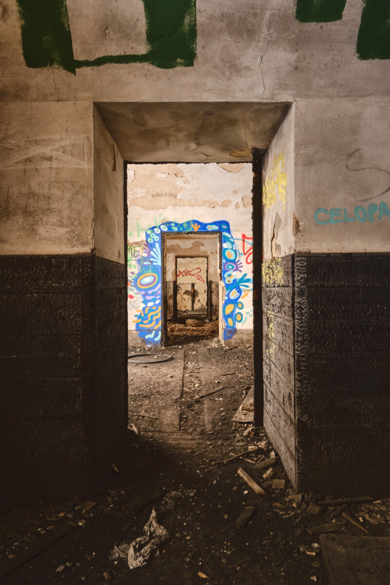 Verlassener Raum mit buntem Graffiti an der Türöffnung, Blick durch mehrere dunkle, beschädigte Türen.