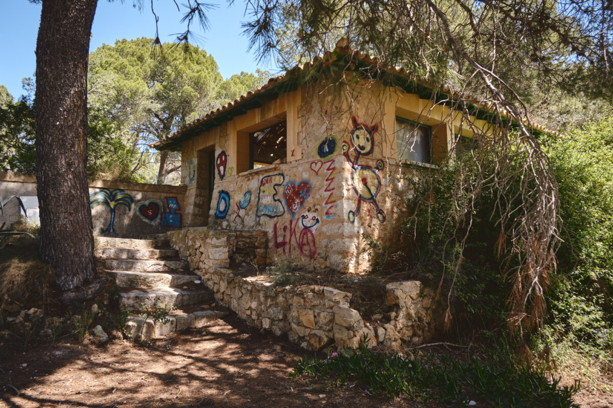 Haus in Waldlandschaft mit bunten Graffitis an den Wänden, umgeben von Bäumen und Natur.