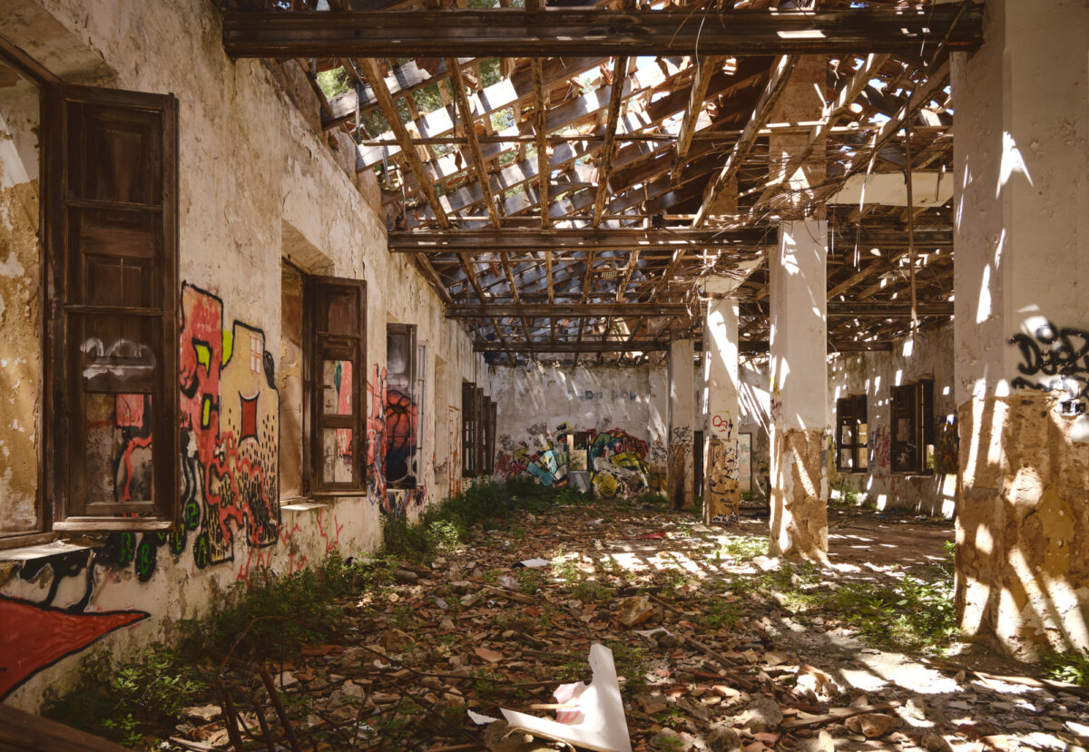 Verfallenes Gebäude mit Graffiti an den Wänden. Sonnenlicht fällt durch das beschädigte Dach auf den Boden.