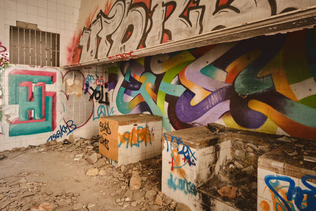 Verlassener Raum mit bunten Graffitis an den Wänden und Schutt auf dem Boden.