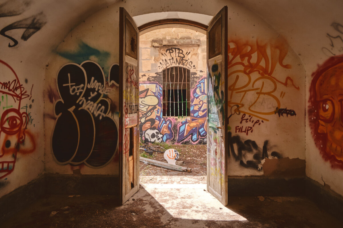 Geöffnete Türen führen zu einem graffiti-bedeckten Innenhof mit bunten Wandbildern und freiem Himmel.