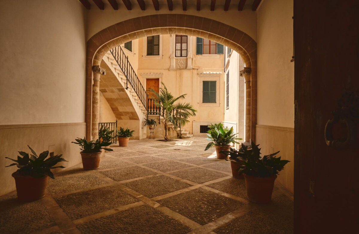 Historischer Innenhof mit Steinboden, Treppe, Pflanzen in Töpfen und Holztüren.
