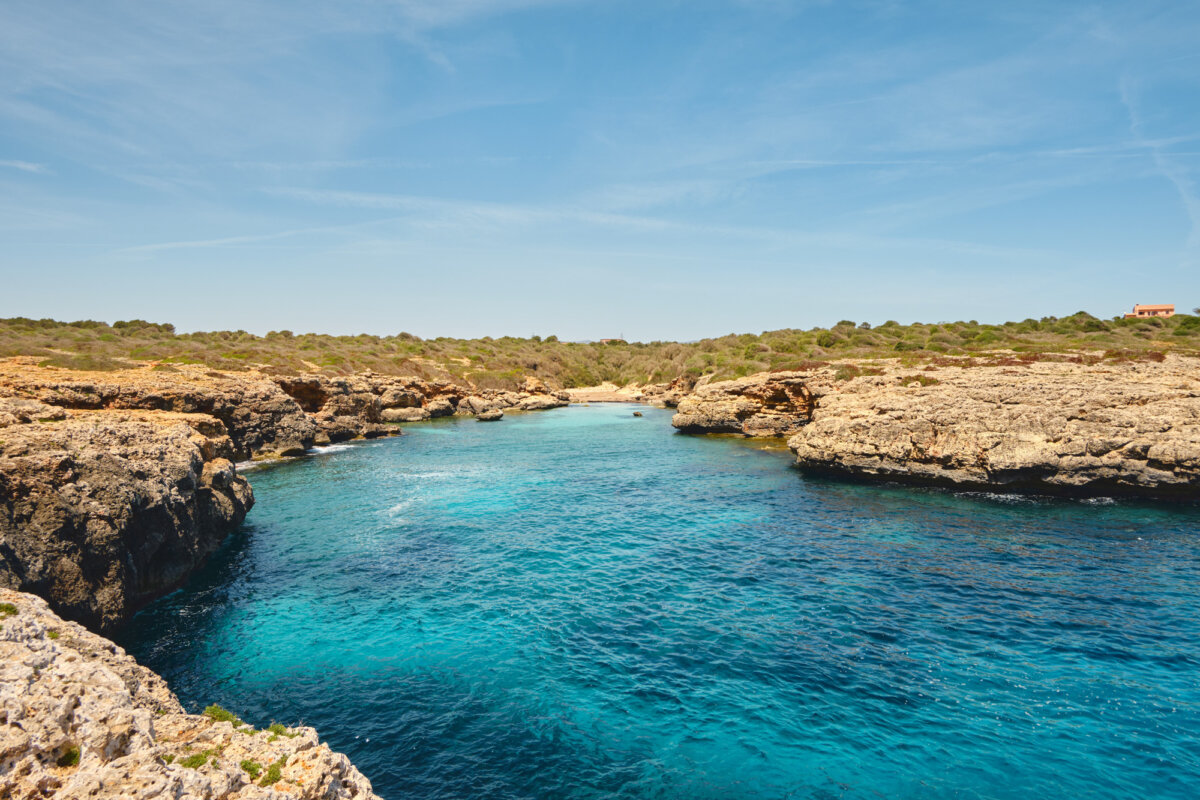 Türkisblaues Meer mit felsigen Küsten und klarem Himmel, im Hintergrund eine grüne Landschaft.