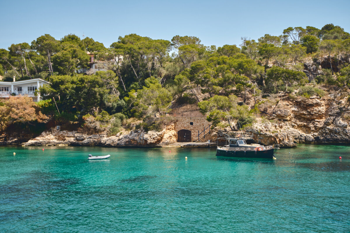 Boot vor felsiger Küste mit Pinien und einem Haus am Meer in Cala Portals auf Mallorca, Spanien.