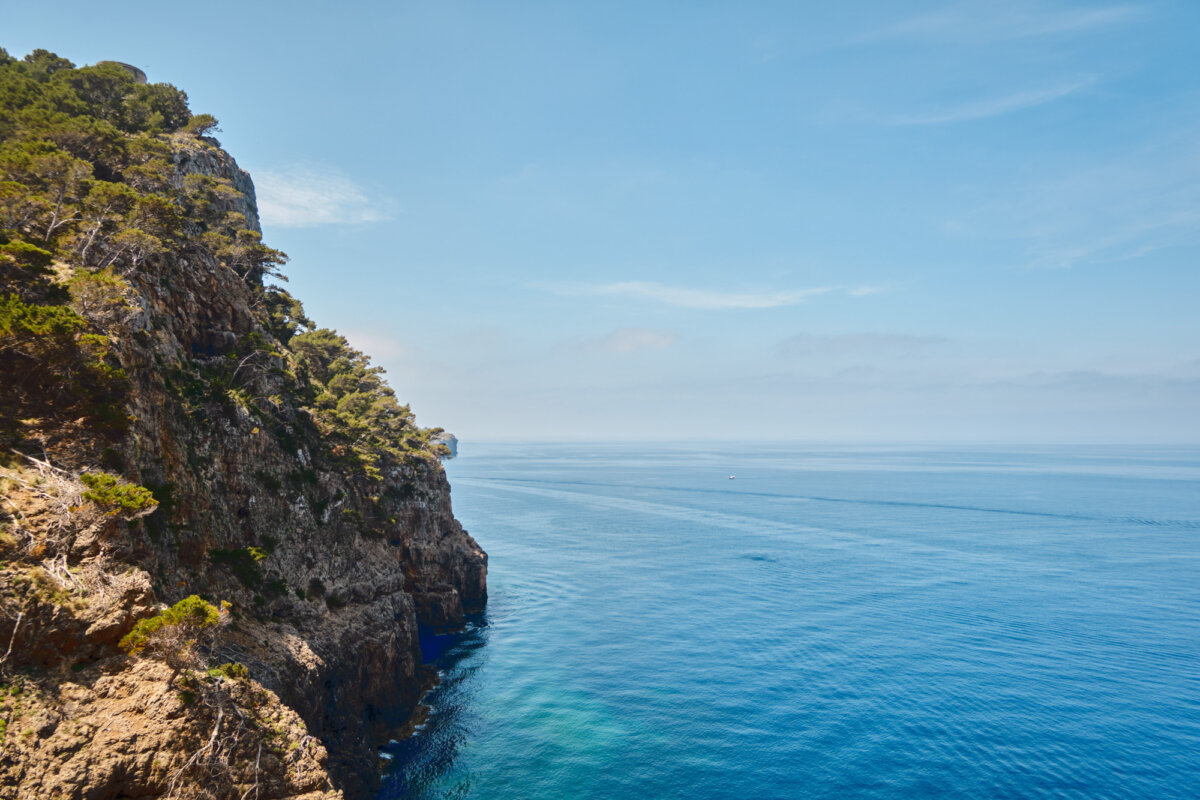 Küste mit klarem blauem Meer und bewachsenen Felsen unter blauem Himmel. Ruhevolle mediterrane Landschaft.