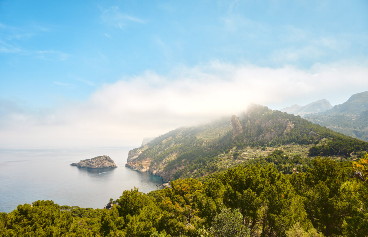 Küste mit grünen Hügeln und blauem Meer unter leicht bewölktem Himmel. Ruhige Landschaft mit dichter Vegetation.