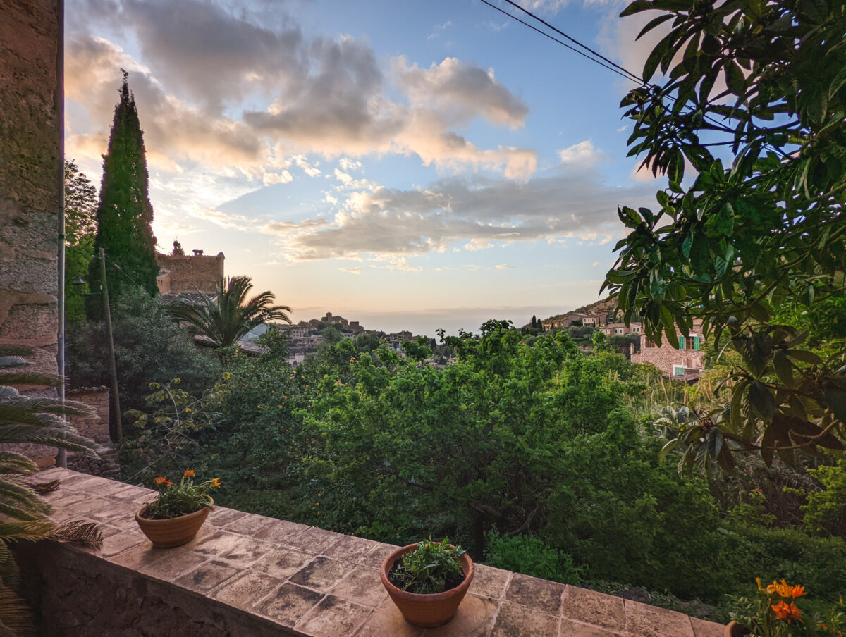 Blick auf eine mediterrane Landschaft mit grünen Bäumen, Gebäuden und einem sonnigen Himmel im Hintergrund.